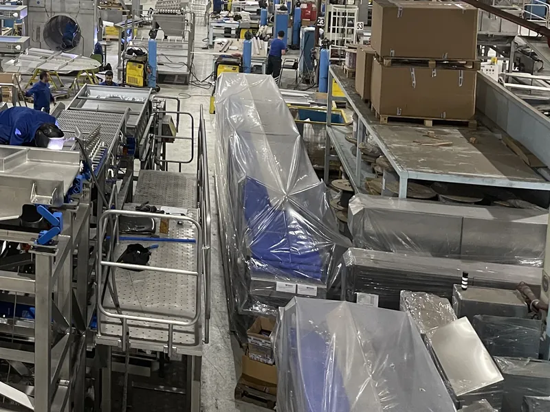 Finished machines wrapped in plastic for shipment beside welding and assembly stations